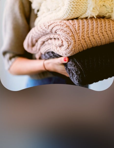 Persona che tiene in mano dei vestiti lavorati a maglia piegati ordinatamente dopo l’asciugatura con l’asciugatrice smart LG