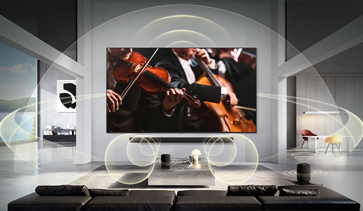 LG Mini RGB evo AI MRGB85 с WOW Orchestra показывает сцену концерта и звуковую панель под экраном, в то время как графическое изображение звуковых волн распространяются по гостиной, изображая синхронизированный объемный звук.