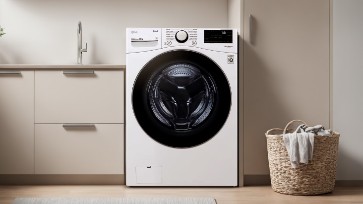 Lavadora de carga frontal LG en el centro, con un gabinete beige a la izquierda y una canasta para ropa sucia a la derecha