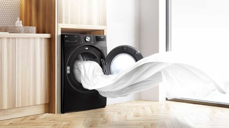 Secadora LG negra con la puerta abierta y una tela blanca ondeando al viento, con un mueble de madera clara a la izquierda