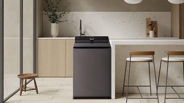Lavadora de carga superior LG gris oscuro en una cocina cálida de tonos neutros con mostrador blanco, mobiliario de madera y taburetes. Lavadora de carga superior LG gris oscuro en una cocina cálida de tonos neutros con mostrador blanco, mobiliario de madera y taburetes.