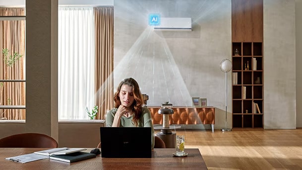 LG DUALCOOL AI airconditioner koelt een vrouw die aan een bureau met een laptop werkt in een woonkamer.