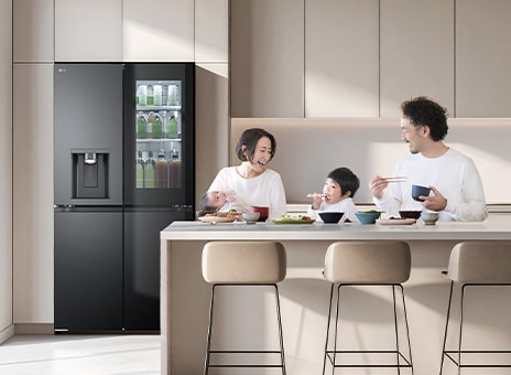 LG's InstaView refrigerator freezer in a bright kitchen. Inside the door is orange juice. A man and a woman are looking at their mother, with a child wearing a white shirt in between.
