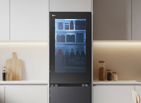LG tall fridge with a see through glass door in a minimalist kitchen. The interior is lit with green lighting, clearly showing stored fresh groceries and beverages.
