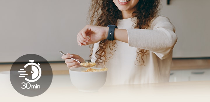 Woman at a table glancing at her wristwatch during a light meal, with a '30 min' icon overlayed on screen