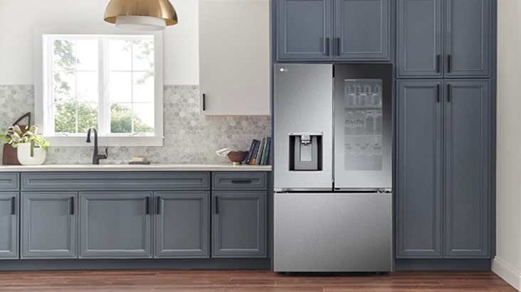 Refrigerador LG con dos puertas en la parte superior y un cajón inferior en una cocina moderna, con panel de vidrio InstaView, dispensador de agua y amplios compartimentos de almacenamiento.