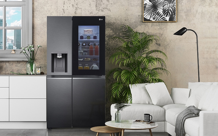 Refrigerador LG de dos puertas colocado en la sala de estar, cerca del sofá, que muestra una solución alternativa cuando el espacio de la cocina es demasiado limitado para mantener una distancia segura con respecto a la cocina.