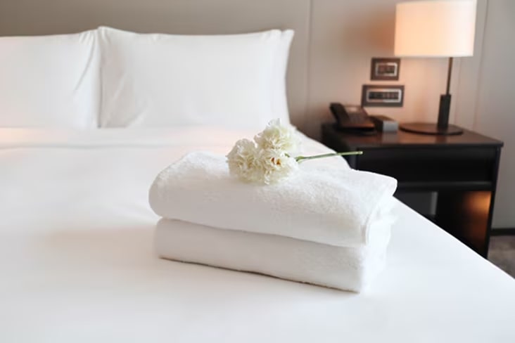 Freshly folded white towels placed on a hotel bed, symbolizing cleanliness and guest comfort	