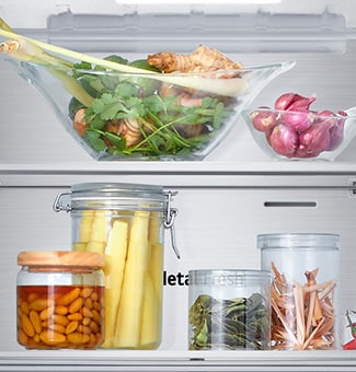 Close-up view of the bottom freezer shelf of an LG with fresh herbs, vegetables and preserves in glass containers.