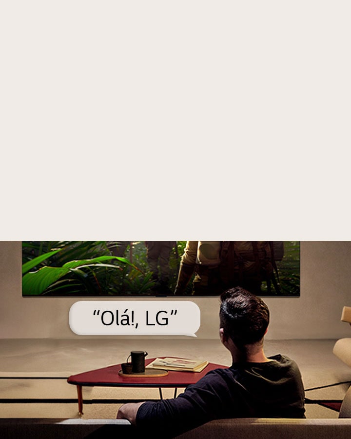 A LG OLED AI B6E com reconhecimento de voz de campo distante é ativada através de um comando de voz quando uma pessoa sentada numa sala diz “Olá, LG” em direção à TV, indicando uma interação de voz mãos livres dentro da interface da TV.
