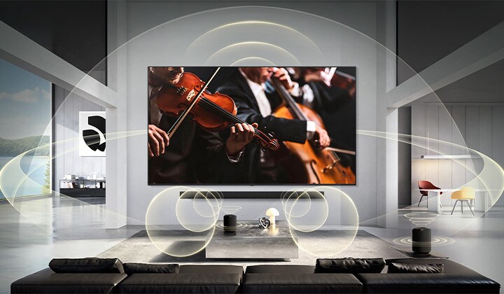 يعرض تلفزيون LG Mini RGB evo AI MRGB9M المزود بخاصية WOW Orchestra مشهد حفل موسيقي مع مكبر صوت Soundbar أسفل الشاشة، بينما تمتد موجات صوتية رسومية عبر غرفة المعيشة لتجسيد صوت محيطي ومتزامن.