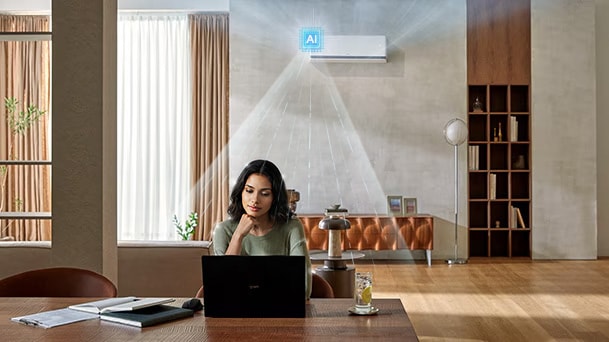 " LG DUALCOOL AI air conditioner cooling a woman working at a desk with a laptop in a living room."