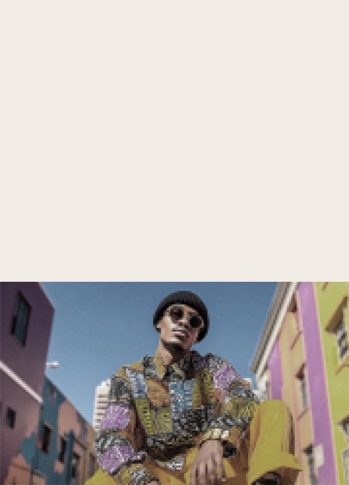 LG QNED AI QNED70 Mini LED with AI Picture Pro shows a low-angle outdoor scene of a man seated between colorful buildings, as AI recognizes the scene and upscales each frame up to 4K for enhanced clarity, texture, and detail.