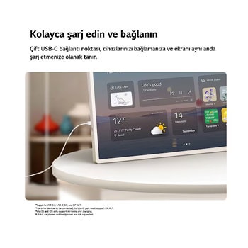LG StanbyME 2 Max LX6 Taşınabilir Ekran, bir masadaki USB-C kablosuyla bağlanarak bir ev widget arayüzünü gösteriyor; sunduğu USB-C bağlantı noktası aracılığıyla rahat şarjı ve sorunsuz cihaz bağlantısını vurguluyor.