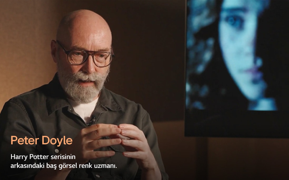 Harry Potter serisinin baş görsel renk uzmanı Peter Doyle, sıcak ve yumuşak ışıklandırılmış bir ortamda el hareketleriyle konuşarak profesyonel ve düşünceli bir atmosfer yansıtıyor.
