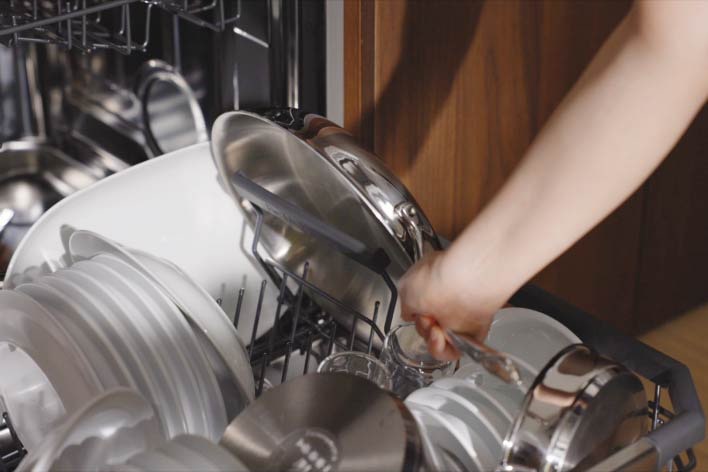 A person unfolds a divider on the side of the dishwasher rack and stores a frying pan upright on its side.