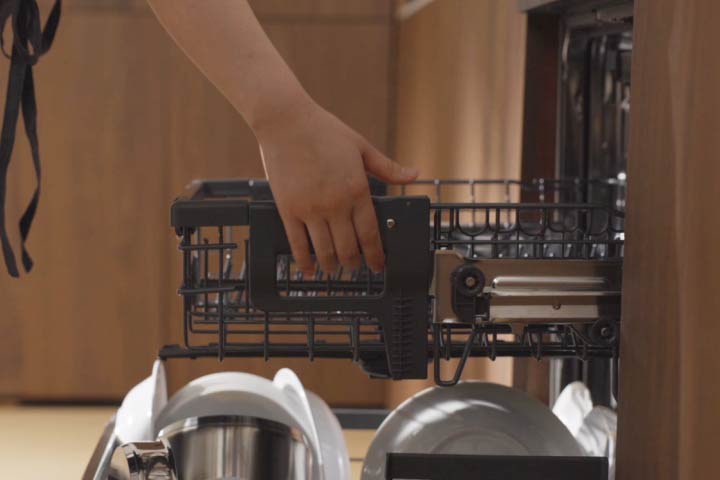 A person raises the dishwasher rack to add more space underneath, then stores frying pans on the lower rack.