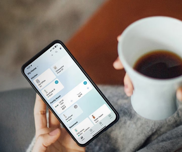 Person holding a smartphone with the LG ThinQ app to monitor and control connected smart home appliances remotely