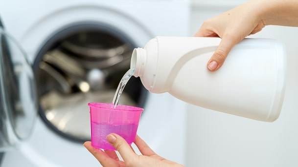 LG front load washing machine with a person pouring liquid washing machine cleaner into a pink measuring cup