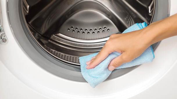 LG front load washing machine with a person wiping the door seal using a blue cloth for regular maintenance