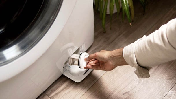 LG front load washing machine with a person removing the bottom drain filter for cleaning and maintenance