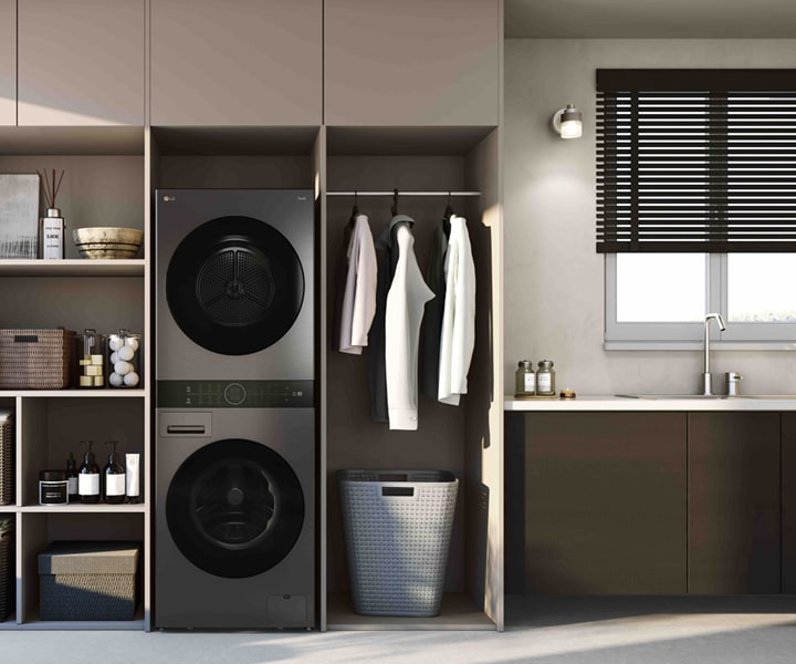 LG WashTower™ in platinum black finish placed in a modern laundry room with shelves, hanging space, and window blinds