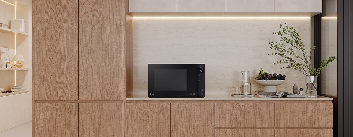 An LG black worktop microwave sits on a light stone worktop with oak cabinets and under-cupboard lighting.