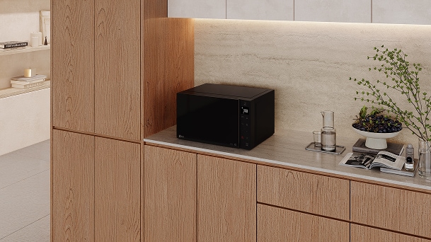 LG black countertop microwave on a light stone counter in a diagonal view with oak cabinets and beige kitchen counter.