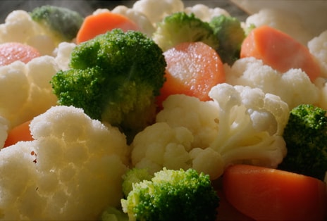 LG microwave food close-up shows broccoli florets, cauliflower, and carrot slices with warm steam lighting.