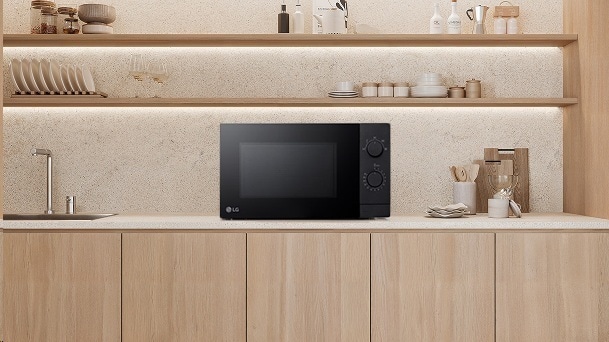 An LG black countertop microwave sits on a light stone counter with pale wood cabinets and open shelves.