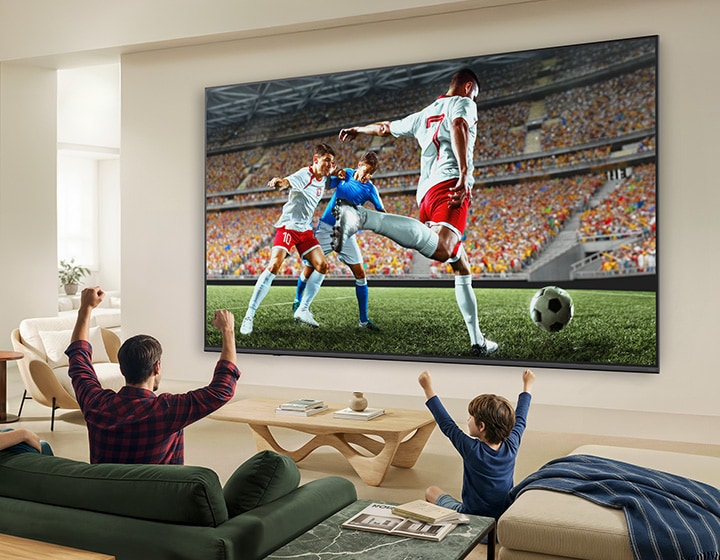 LG QNED evo AI QNED83 Mini LED Ultra Big TV shows an intense, large-scale soccer play with refined picture quality and vivid colours as a family cheers together from sofas in a living room.