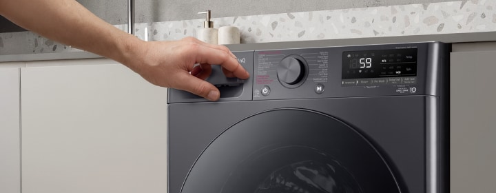 Máy giặt cửa trước LG với bàn tay điều chỉnh nút xoay nhiệt độ trong không gian giặt giũ hiện đại kiểu nhà bếp	