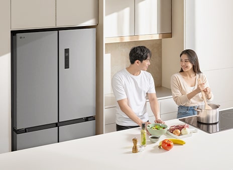 Tủ lạnh LG màu xám đậm dung tích lớn với không gian lưu trữ rộng rãi trong một căn bếp phong cách. Một người đàn ông và một người phụ nữ đang nấu ăn trước bàn.