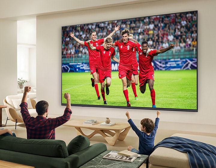 LG QNED evo AI QNED80 Mini LED Ultra Big TV được treo tường trong phòng khác ngập tràn ánh sáng, tái hiện trọn vẹn khoảnh khắc ăn mừng chiến thắng của trận bóng đá với màu sắc sống động và chất lượng hình ảnh vượt trội trên màn hình lớn, khi cả gia đình ngồi trên sofa cùng nhau cổ vũ.