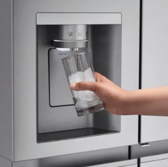 A hand fills a glass with ice cubes from the built-in dispenser of an LG fridge freezer. Ice is coming out of the dispenser located on the front of the refrigerator door.