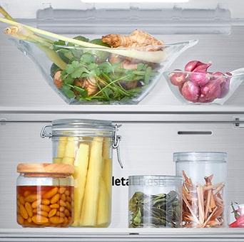 Close-up view of the bottom freezer shelf of an LG with fresh herbs, vegetables and preserves in glass containers.