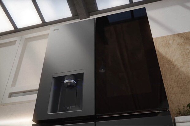 Close-up of black LG InstaView fridge freezer with matte finish. Sunlight from a window above highlights the surface. A built-in water dispenser is on the left side of the door.	