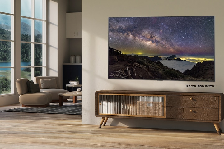 Innenansicht eines Landhauses. Ein riesiger, an der Wand befestigter LG TV zeigt auf seinem Bildschirm ein wunderschönes Naturlandschafts-Artwork. Der Fernseher sieht aus wie ein Foto, das an der Wand hängt. 