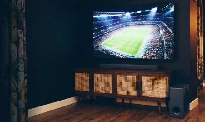 Large TV showing a soccer match above a wooden TV stand in a cozy living room.