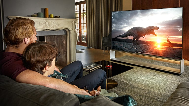 Vater und Sohn sehen eine Dinosaurier-Dokumentation auf einem Großbildfernseher