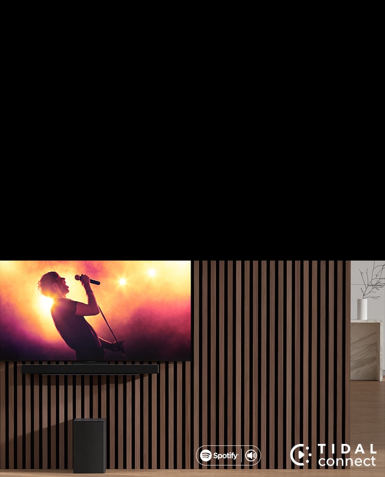 LG TV shows a concert, and LG Sound Bar is placed below LG TV. On the left, sub-woofer is on the brown shelf.