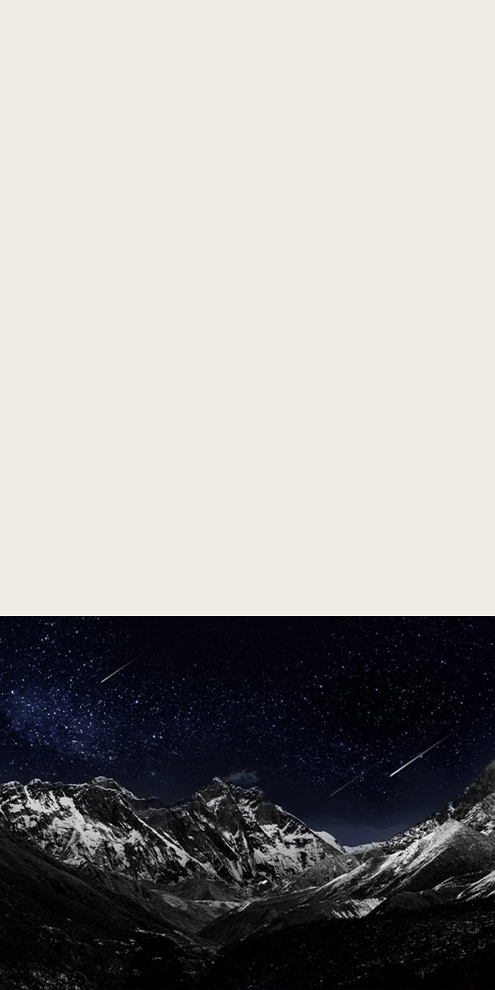 Living room space with a wall-mounted LG OLED TV. On the TV is a mountain range against a dark evening sky filled with stars.