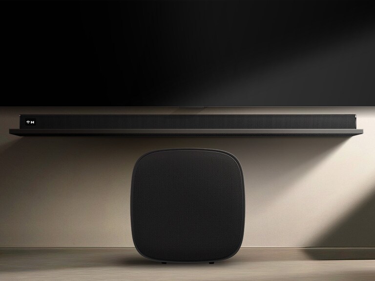 LG Sound Suite W7 woofer placed below a TV with a soundbar, showing easy wireless sound expansion for an immersive home stereo audio system