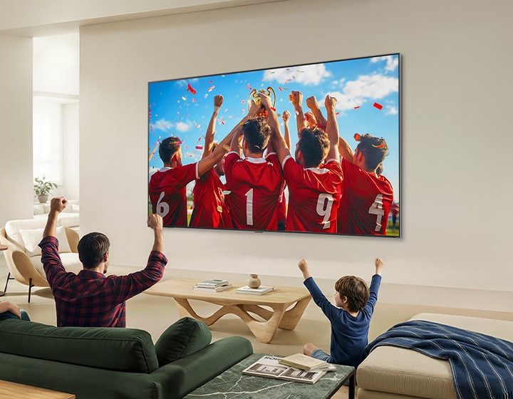 LG QNED evo AI QNED85 Mini LED Ultra Big TV is wall-mounted in a living room, displaying a sports victory celebration with vivid colors and refined picture quality across the wide screen as a family seated on sofas cheers together.