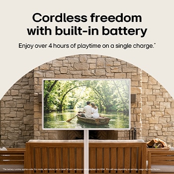 LG StanbyME 2 Max LX6 Movable Screen with a Built-in Battery stands among wooden furniture in a stone-walled courtyard, supporting over four hours of playback in one charge for flexible viewing without a power connection.