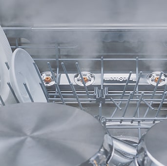 Close-up of dishes and glasses being steam-washed inside dishwasher.