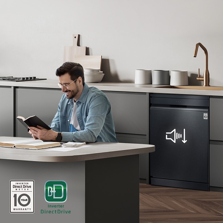 A man reading a book at the kitchen island while the LG free-standing Dishwasher is running in the background.