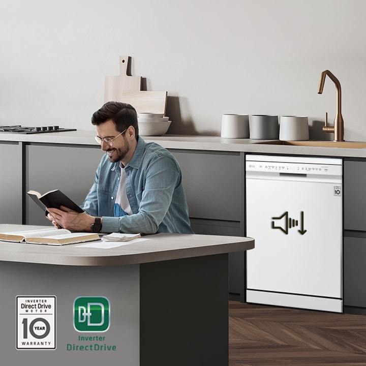 A man reading a book at the kitchen island while the LG free-standing Dishwasher is running in the background.