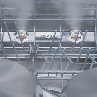 Close-up of dishes and glasses being steam-washed inside dishwasher.