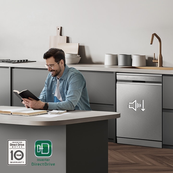 A man reading a book at the kitchen island while the LG free-standing Dishwasher is running in the background.